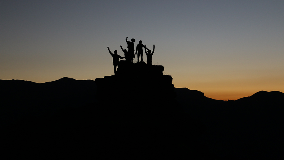 silhouette of team members at the top of a peak