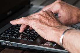 older man's hands typing on a laptop computer