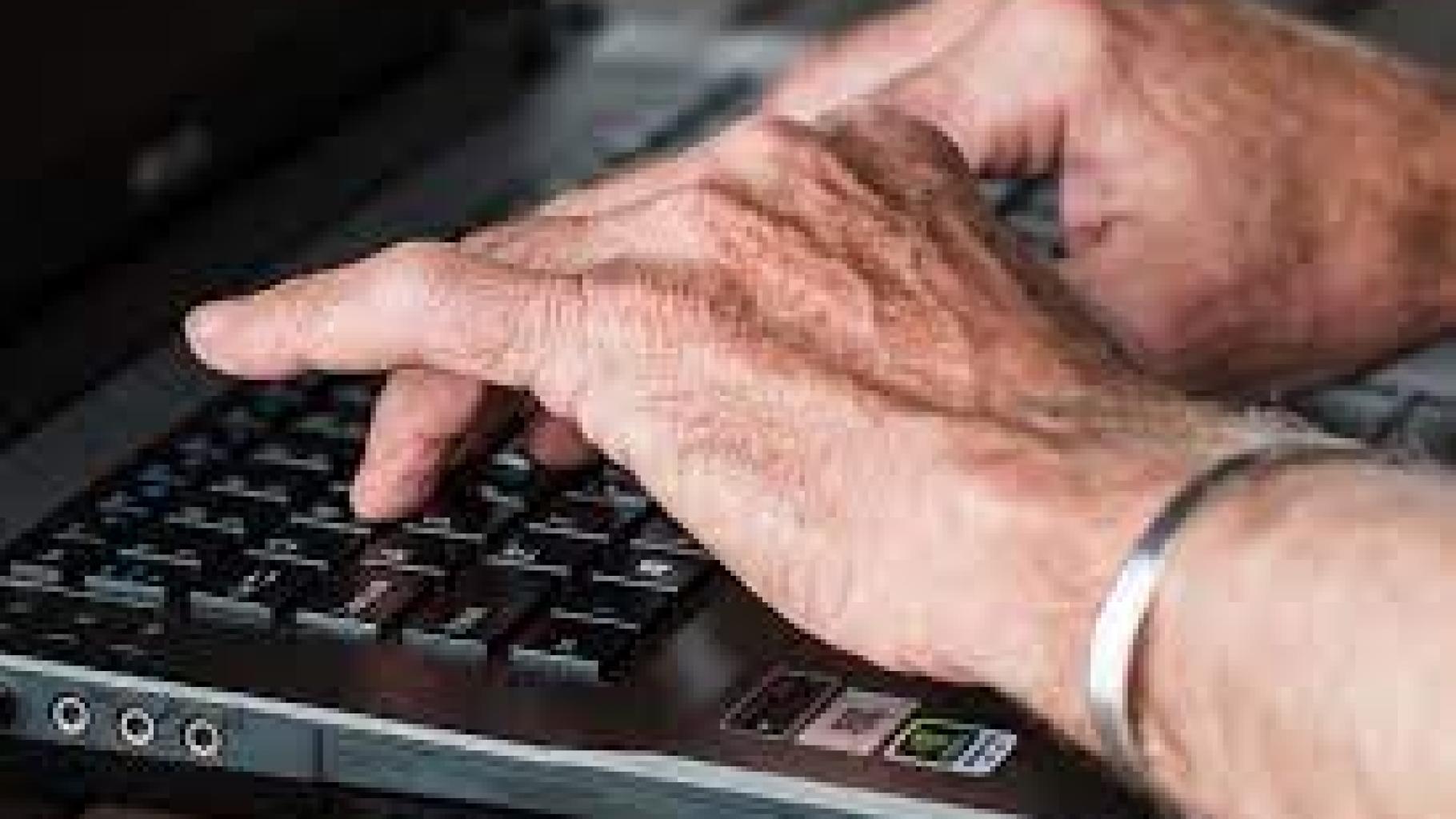 older man's hands typing on a laptop computer